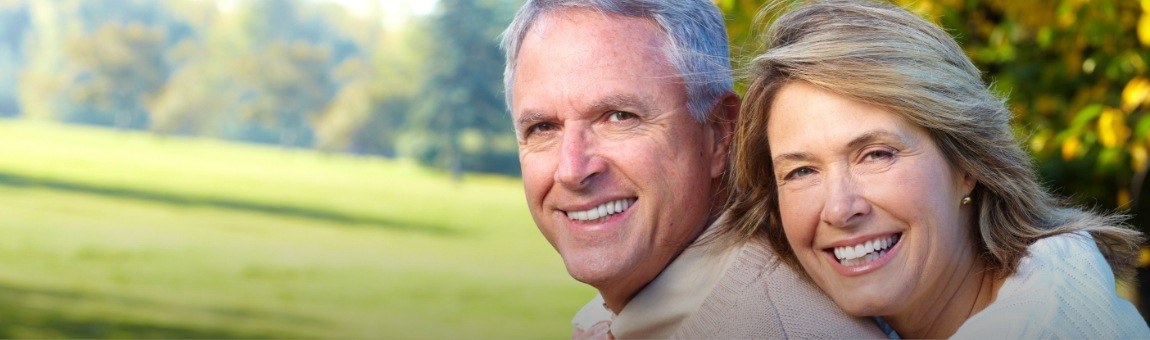 Man and woman smiling after dental bridge supported tooth replacement