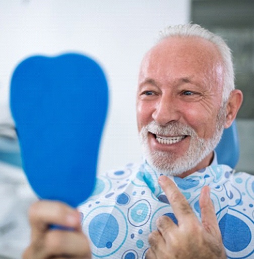 man admiring his new implant denture in a mirror