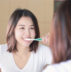 woman looking in the mirror while brushing her teeth  