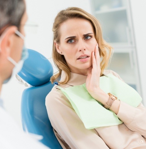 Woman in dental chair for root canal holding cheek in pain