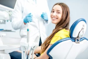 Woman in yellow shirt smiling while sitting in dental chair
