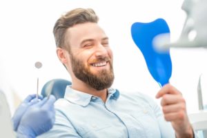 Man smiling in dental chair looking in dental mirror